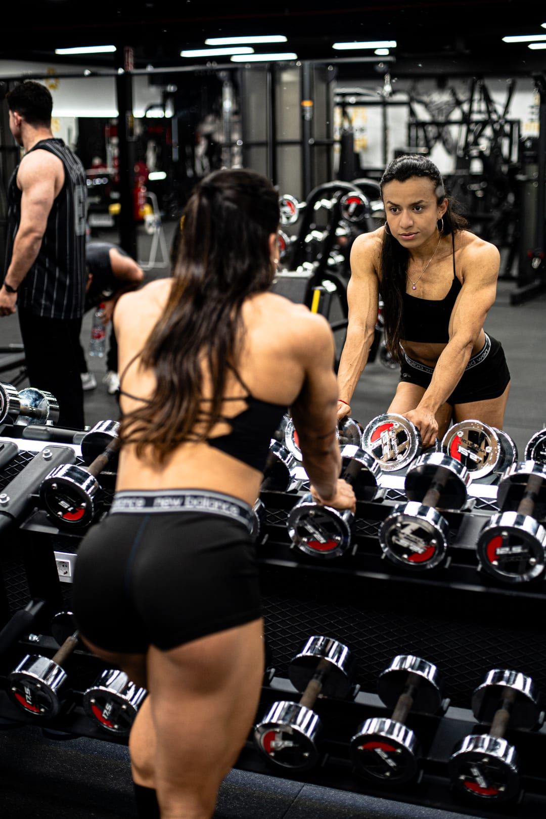 Chery Figueroa entrenando con una atleta del equipo junto al rack de mancuernas del gimnasio